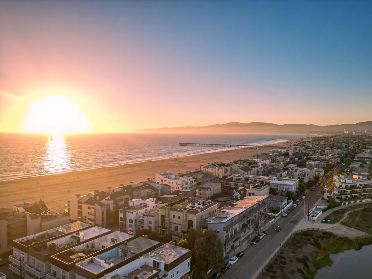 Aerial view of Venice, California, featuring beachfront homes, the Pacific Ocean, Venice Beach, and the iconic Venice Fishing Pier at sunset