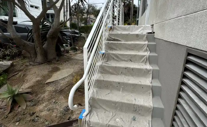 Concrete staircase with white metal railing wrapped in protective plastic sheeting during exterior restoration, Marina del Re