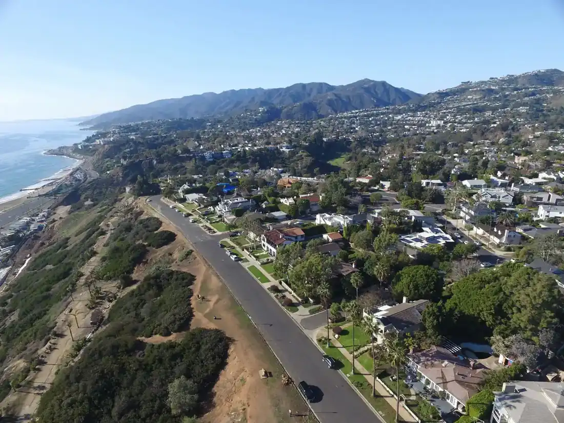 Wide aerial view of Pacific Palisades, California, showcasing coastal neighborhoods, scenic bluffs, the Pacific Ocean, and the Santa Monica Mountains.