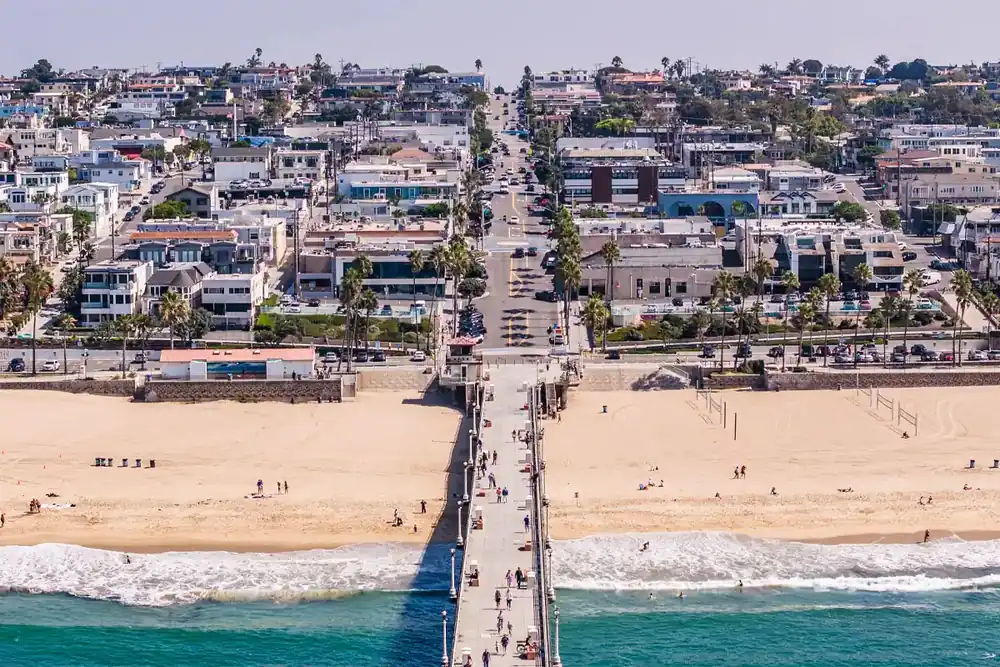 Wide aerial view of Manhattan Beach, California, featuring the Manhattan Beach Pier, Pacific Ocean, beachfront homes, and surrounding neighborhood