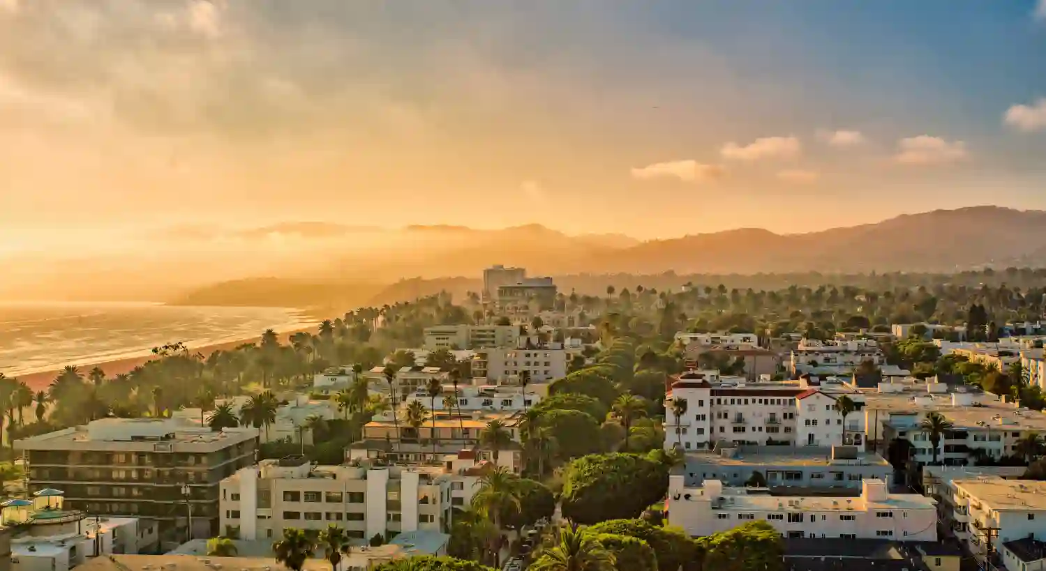Hazy sunset over Santa Monica rooftops and palms, with the bay and mountains beyond