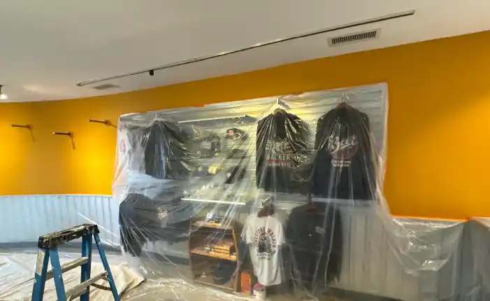 Retail interior with a mustard yellow curved wall and merchandise shelving covered in plastic during commercial renovation work
