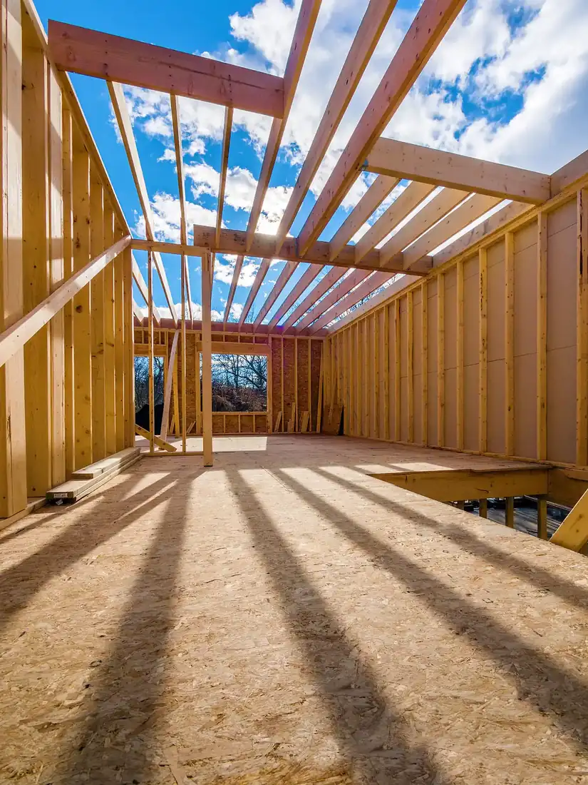 Structural framing for a custom home under construction showing roof trusses, engineered framing, and load-bearing walls before roofing and exterior finishes are installed